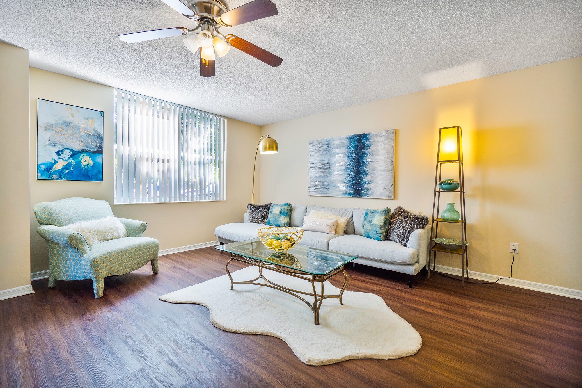 A living room with a blue chair, a white couch, and a glass coffee table.